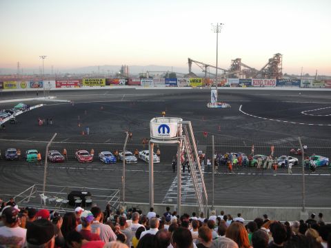 1998 Ford Crown Victoria - Cars are lined up on a race track with a Mopar tower in the foreground and industrial structures in the background.