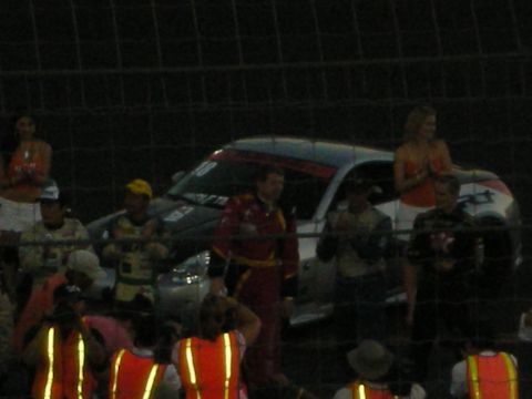 1998 Ford Crown Victoria - A race car is parked behind a fence with several people gathered around, some appearing to be crew members.