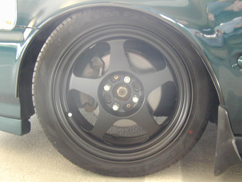 Black five-spoke wheel on a green car, low-profile tire, brake caliper visible