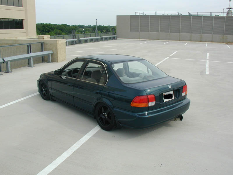 Dark green Honda Civic sedan, lowered on black wheels, rear three-quarter on a parking deck