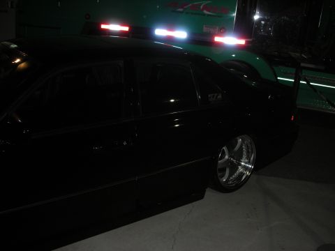 1998 Ford Crown Victoria - A black sedan with custom wheels is parked next to a large green truck at night.