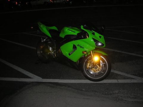 1998 Ford Crown Victoria - A bright green Kawasaki Ninja motorcycle is parked in a lot at night, with its front wheel and fairing illuminated.
