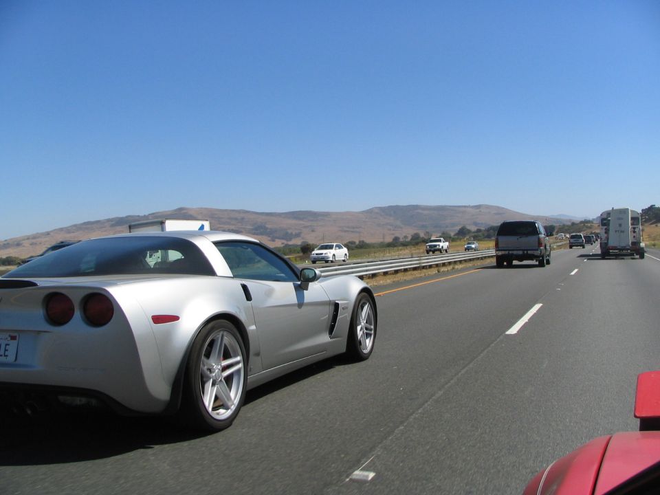 Silver sports car on highway, rear quarter view. Visible taillights, alloy wheels, and a partial license plate