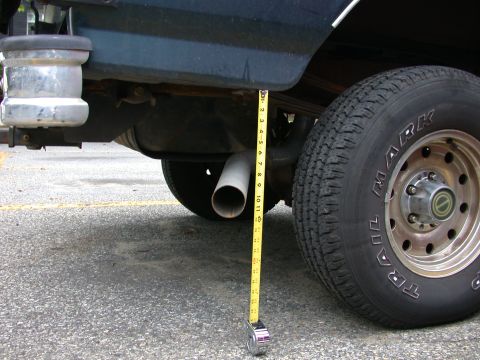 1995 Ford Bronco - A tape measure is used to measure the clearance of the exhaust pipe from the ground, next to the rear tire of a vehicle.