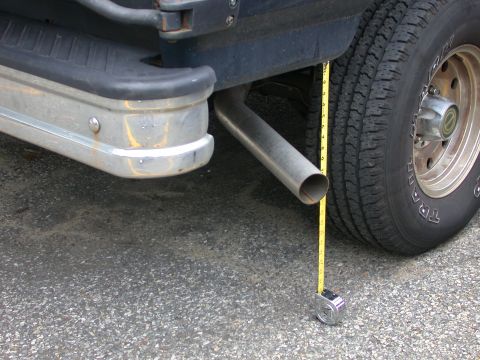 1995 Ford Bronco - A tape measure is used to measure the exhaust pipe of a vehicle, positioned near the rear bumper and tire.