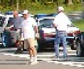 1993 Ford Mustang - Three men stand beside two cars in a parking lot on a sunny day.