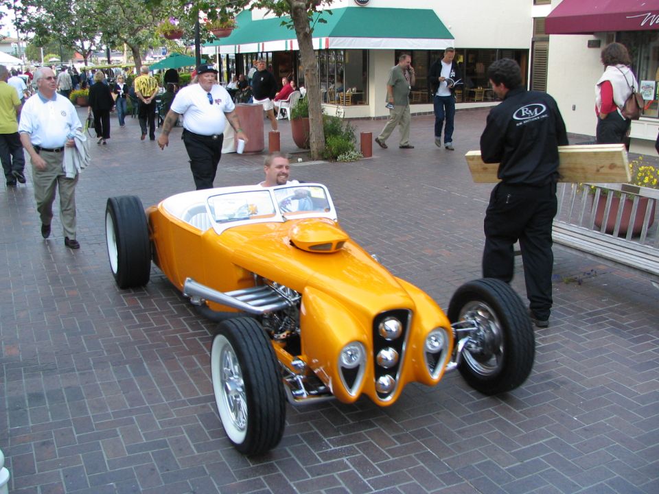 Orange custom hot rod roadster with exposed engine pipes and a scoop on the hood