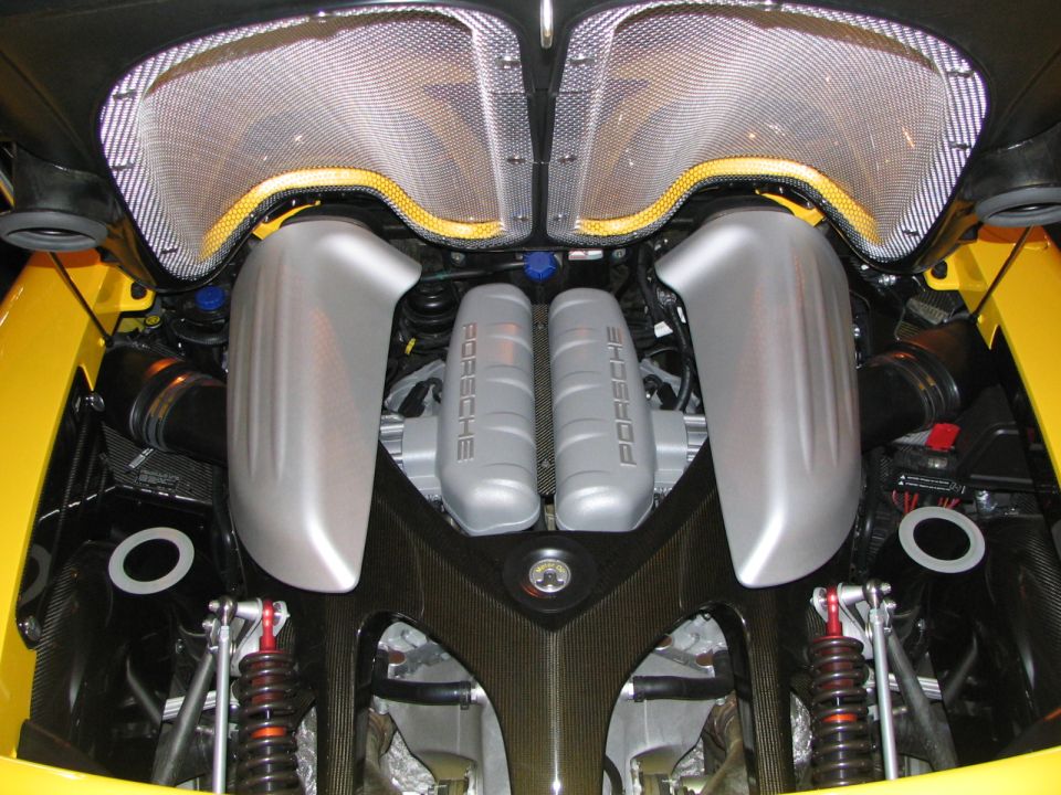 Close-up of a yellow Porsche's engine bay, showing twin silver engine covers with 'PORSCHE' embossed on them