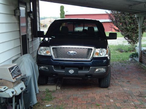 2005 Ford F-150 - This dark blue 2005 Ford F-150 truck is parked under a covered area, showing its distinctive chrome grille and front end.