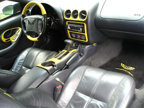 1984 Pontiac Fiero - The interior features black leather seats and yellow accents on the dashboard and steering wheel, with a 'Trans Am' floor mat visible.