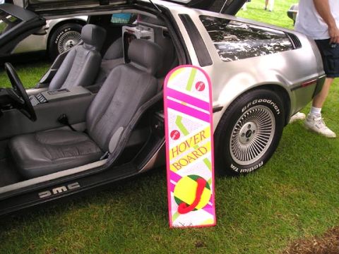 1984 Pontiac Fiero - A DeLorean DMC-12 is parked on grass with a hoverboard prop. Another vehicle is in the background.