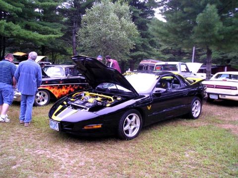 1984 Pontiac Fiero - A black 1994 Pontiac Firebird is displayed with its hood open, revealing the engine bay, at an outdoor car show.