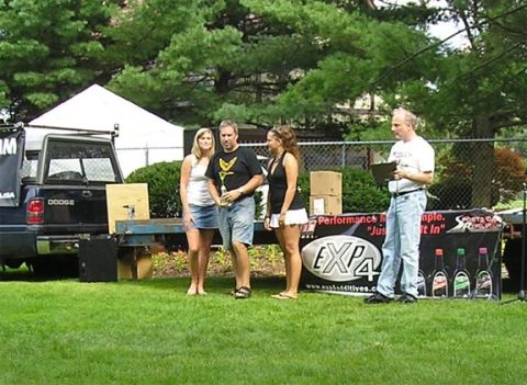 1984 Pontiac Fiero - A black Dodge pickup truck is seen from the rear at an outdoor event with people and a promotional display.