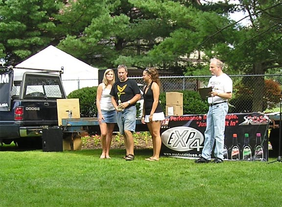 Black Dodge pickup truck rear view, parked on grass with people and a display table