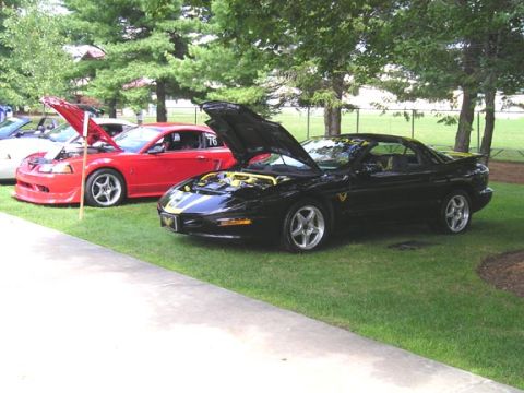 1984 Pontiac Fiero - A black 1994 Pontiac Fiero is parked on the grass with its hood open, next to a red Ford Mustang.