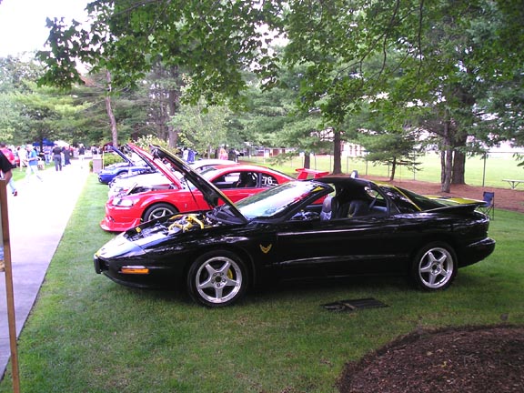 Black 1994 Pontiac Firebird with hood open, parked on grass at car show