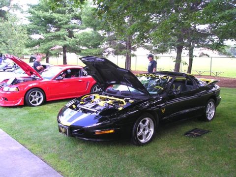 1984 Pontiac Fiero - A black 1994 Pontiac Firebird Trans Am is displayed with its hood open, revealing yellow engine accents.