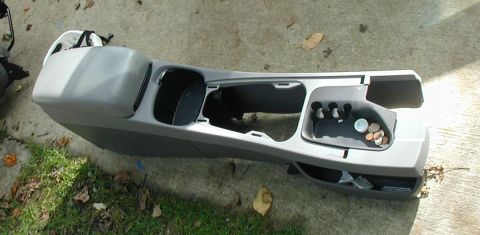2000 Ford Taurus - A gray center console removed from a sedan and set on a concrete walkway, viewed from above with the padded armrest lid, shifter opening, c…