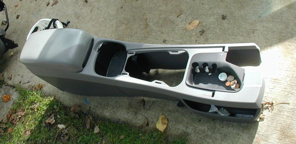 Gray sedan center console removed and sitting on concrete, coins in the tray