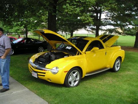 1984 Pontiac Fiero - A yellow retro pickup truck with its hoods open is parked on the grass next to a black car.