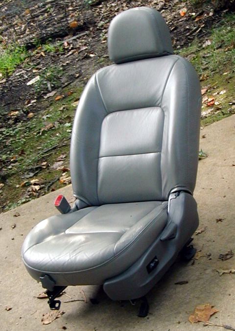2000 Ford Taurus - A gray leather power driver's seat removed from a car and standing on a concrete driveway, with the headrest installed, red seatbelt buckle…