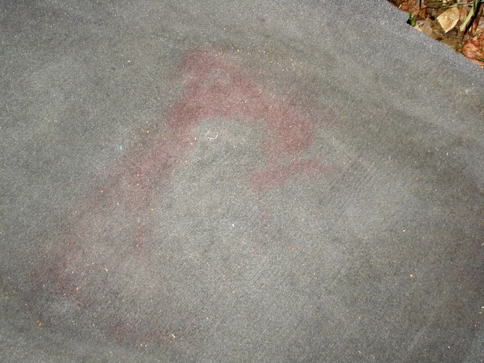 Gray car carpet removed from vehicle with a large reddish stain in the pile