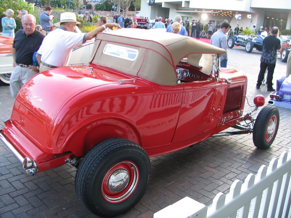 Red convertible hot rod with tan top, chrome bumper, and exposed engine components
