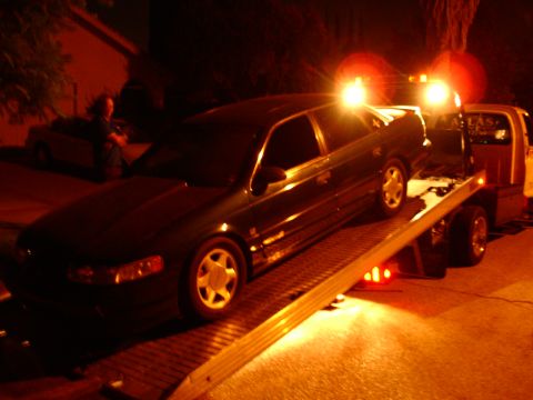 1993 Ford Taurus - A dark-colored 1993 Ford Taurus is loaded onto a flatbed tow truck at night.