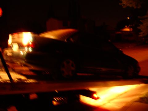 1993 Ford Taurus - A dark sedan is loaded onto a tow truck at night, with its taillights illuminated.