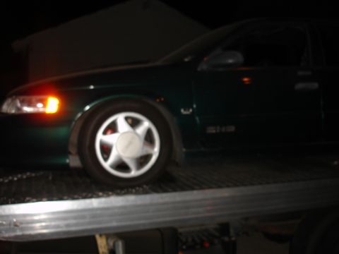 1993 Ford Taurus - A green 1993 Ford Taurus is loaded onto a tow truck at night.