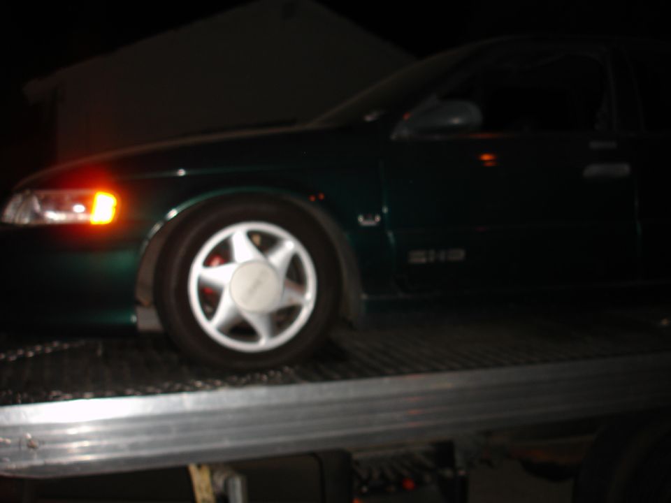 Green 1993 Ford Taurus sedan on a tow truck, side view, with a star-shaped wheel cover