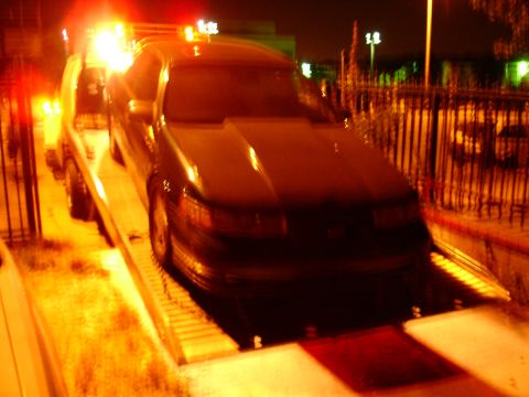 1993 Ford Taurus - A dark sedan is being towed at night, with its front end visible on the flatbed.