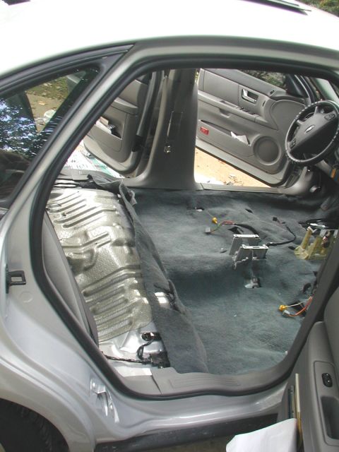 2000 Ford Taurus - Rear compartment of a silver Ford sedan with the rear bench removed, exposing the bare painted floor pan behind the seat and gray carpet wi…