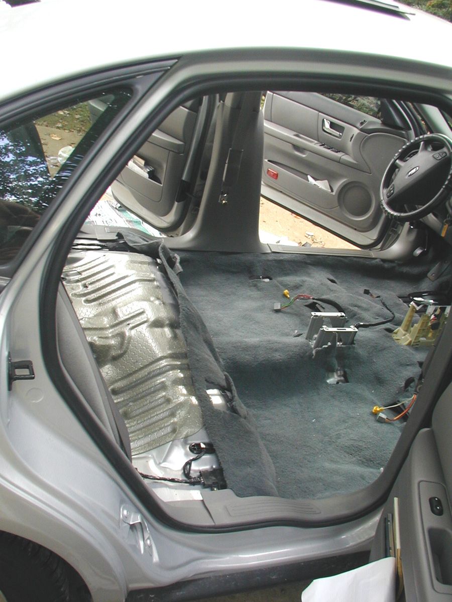 Ford sedan rear seat removed, bare floor pan and loose wiring on gray carpet