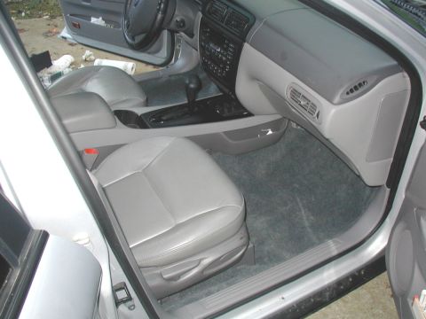2000 Ford Taurus - Passenger-side interior of a silver Ford sedan shot through the open front door, showing reassembled gray leather front seats, freshly fitt…