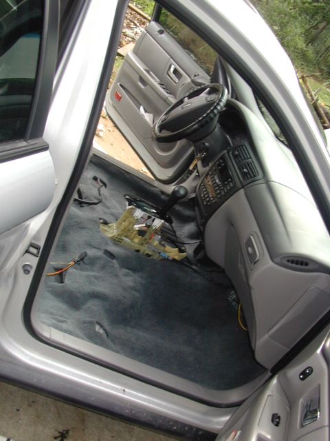 2000 Ford Taurus - Front interior of a silver Ford sedan stripped of its seats and center console, shot through the open passenger door and showing bare gray…