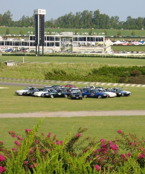 1993 Ford Mustang - Multiple vehicles gathered on the infield of a racetrack, with grandstands visible.