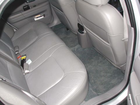 2000 Ford Taurus - Rear bench seat of a sedan in gray leather, photographed through the open rear door with the reinstalled gray floor carpet clean and taut a…