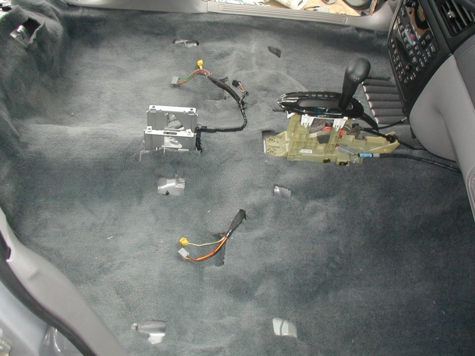 Stripped car floor with new gray carpet, exposed shifter, module and loose wiring harness