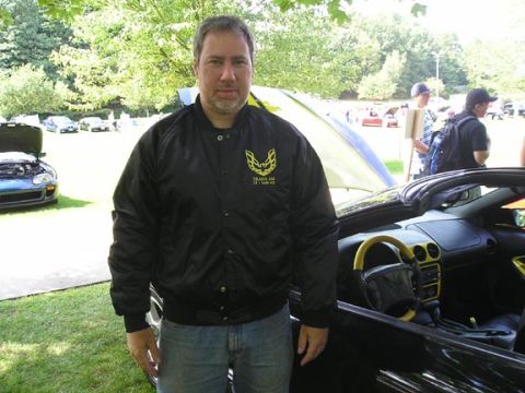 1984 Pontiac Fiero - A man stands by a black convertible with a yellow interior, while other vehicles are visible in the background.