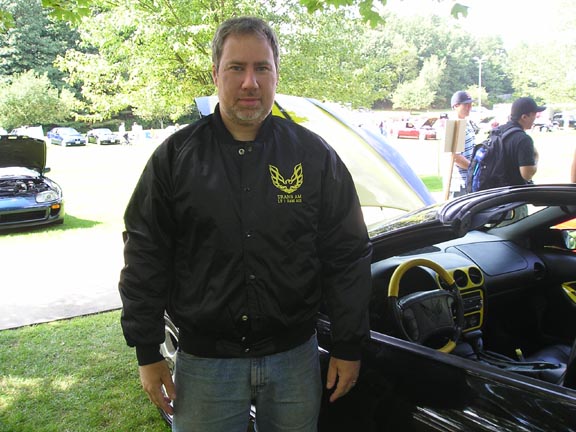 Black convertible interior with yellow accents, man in Trans Am jacket, other cars in background