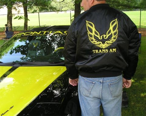 1984 Pontiac Fiero - A person wearing a Trans Am jacket stands next to a car with racing stripes and 'Pontiac' text on the windshield.