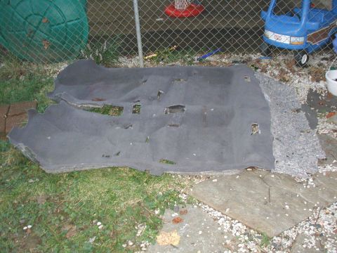 2000 Ford Taurus - The old molded gray floor carpet pulled from a car and laid upside down on the grass in a backyard, showing the jute backing, seat-mount cu…