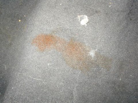 2000 Ford Taurus - Close-up of a reddish-brown stain soaked into gray automotive carpet, photographed with flash so the fibers and stray white threads stand o…