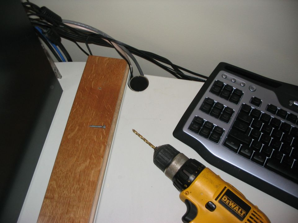 Yellow drill with a bit pointed at a wooden beam next to a computer keyboard