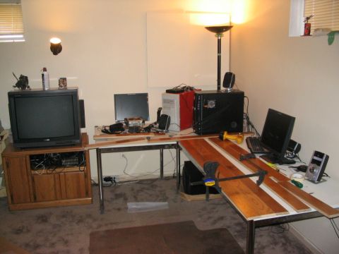 1986 Ford Bronco - A cluttered workspace features computers, electronics, and unfinished wood planks on a desk.