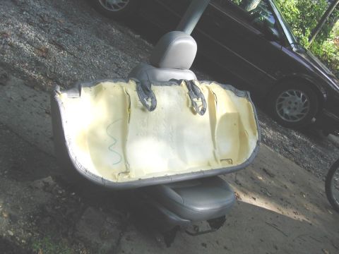 2000 Ford Taurus - A gray leather front seat sits removed on a driveway with its seatback cover peeled off, exposing the yellow molded foam cushion, headrest…