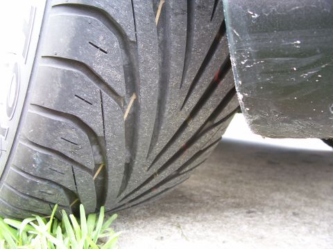 1994 Ford Probe - A close-up view of a tire tread on a vehicle, with grass and concrete visible in the background.