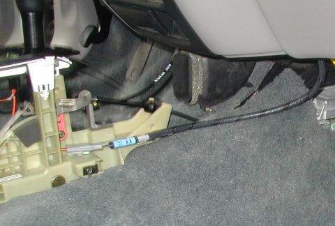 2000 Ford Taurus - The automatic shifter assembly on a car's floor tunnel with its console trim removed, exposing the tan plastic base, black shift lever, red…