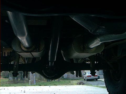 1978 Ford Bronco - Underside view of a vehicle's exhaust system and rear axle, with another car in the background.